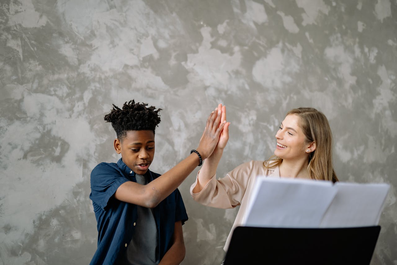 Home A child and teacher celebrate success with a high five during piano lessons, ensuring a positive learning environment.